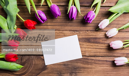 Tulips forming frame around white card on wooden table