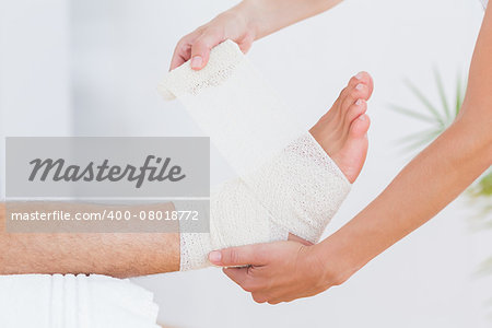 Doctor bandaging her patient ankle in medical office