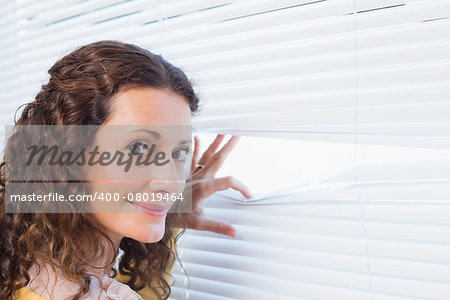 Curious woman looking through blinds in the house