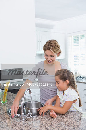 Mother and daughter filling pot with water at home in kitchen