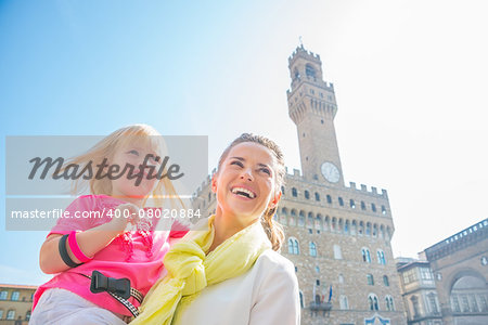 Happy mother and baby girl looking into distance in front of palazzo vecchio in florence, italy