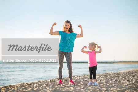 Healthy mother and baby girl showing biceps on beach