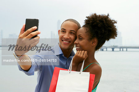 Black tourist heterosexual couple in Casco Antiguo Panama City with shopping bags. The man takes a selfie with his girlfiend and shopping bags with skyline in background