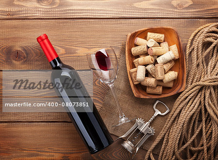 Red wine bottle, wine glass, bowl with corks and corkscrew. View from above over rustic wooden table background