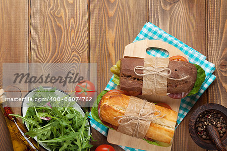 Two sandwiches with salad, ham, cheese and tomatoes on wooden table. Top view with copy space