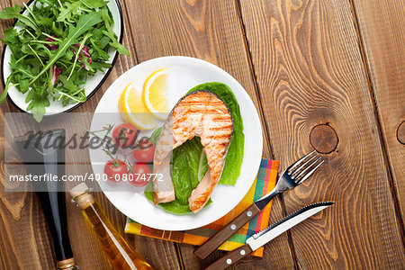 Grilled salmon, salad and condiments on wooden table. Top view with copy space