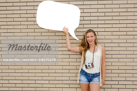 Beautiful and young teenager holding a thought balloon, in front of a brick wall