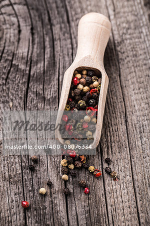 Wooden spoon full of mix pepper on a rustic wooden background