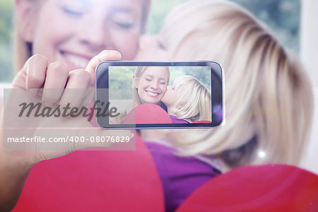 Hand holding smartphone showing against happy mother and daughter on the couch with heart card
