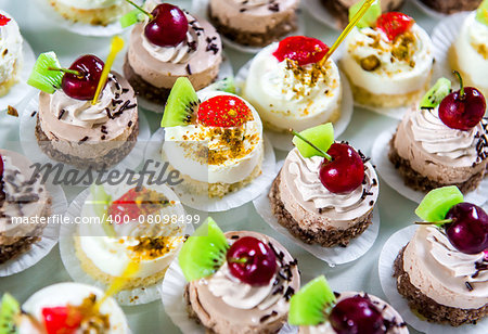 Delicious small fancy cakes decorated with cherry, kiwi and strawberries