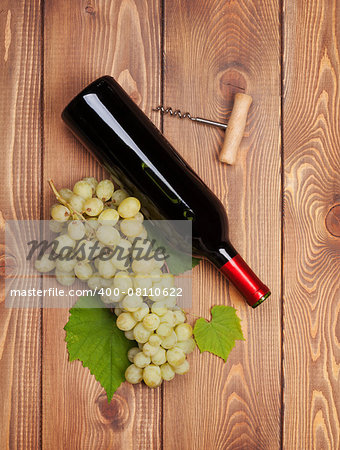 Red wine bottle and bunch of white grapes on wooden table background