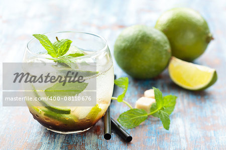 Fresh mojito cocktail on bamboo placemat. Over blue rustic background. Focus on  frontal part of glass, lime and mint leaves in it.