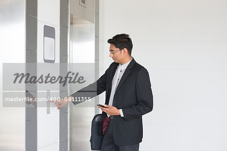 Asian Indian businessman pressing on elevator button, waiting door open to enter inside the lift.