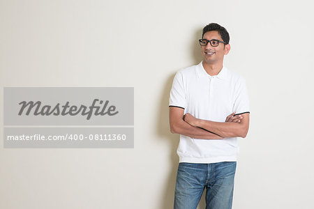 Portrait of handsome Indian guy standing on plain background, looking at copy space at side.
