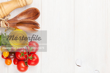 Fresh colorful tomatoes, basil and olive oil on white wooden table. Top view with copy space