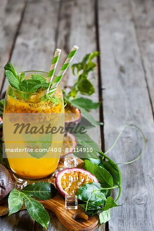 Homemade lemonade with passionfruit, mint leaves and ice cubes on old wooden background. Copy space background.