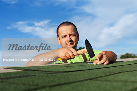 Man finishing installing the bitumen roof shingles - fastening the last pieces with nails and hammer