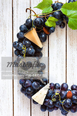 Red wine grape wreath decorated cheese, nuts and old corkscrew hanging on wooden board with place for text or invitation. Vintage style.