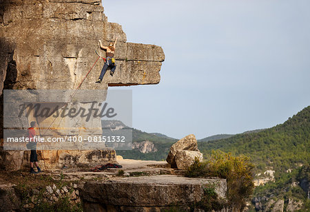 Young woman climbing on cliff, male partner belaying