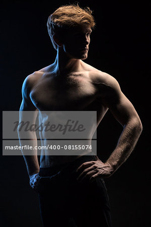 Portrait of handsome red-haired athlete topless at the studio on a black background in low key