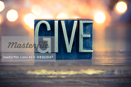 The word GIVE written in vintage metal letterpress type on a soft backlit background.