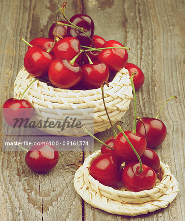 Two Wicker Bowls with Ripe Sweet Cherries isolated on Rustic Wooden background. Retro Styled