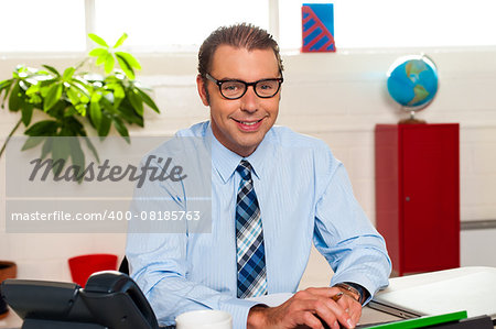 Portrait of a bespectacled businessman sitting in his office and working on documents.