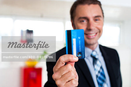 Businessman in formals holding up his credit card and showing to the camera.