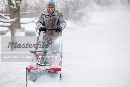 Man using snowblower to clear deep snow on residential driveway after heavy snowfall