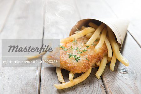 Fish and chips. Fried fish fillet with french fries wrapped by paper cone, on wooden background.