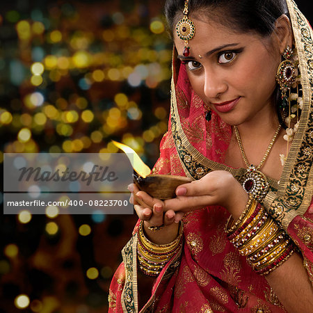 Indian girl in traditional sari lighting oil lamp and celebrating Diwali or deepavali, fesitval of lights at temple. Woman hands holding oil lamp, beautiful lights bokeh background.