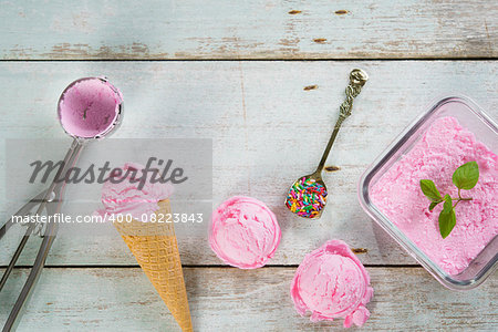 Top view pink ice cream in waffle cone with utensil on rustic wooden background.