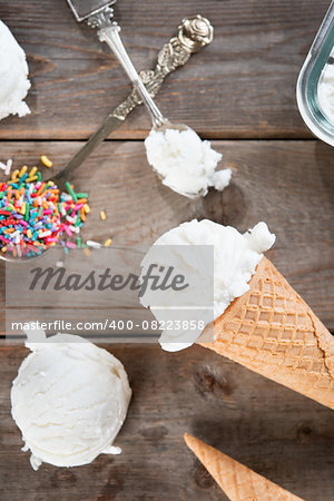 Top view scoop vanilla ice cream in waffle cone with spoon and color rice on wood background.