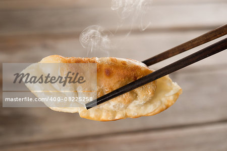 Close up fresh pan fried dumpling with chopsticks. Chinese food with hot steams on rustic vintage wooden background.