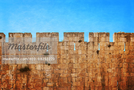 Defensive wall of the ancient holy Jerusalem, lit by the bright sun. Photo in old color image style.