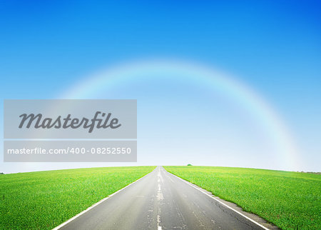 Summer landscape with endless asphalt road through the green field and blue sky with rainbow