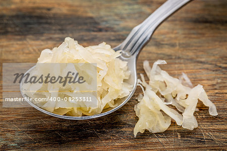 tablespoon of sauerkraut against rustic wooden cutting board - healthy eating concept