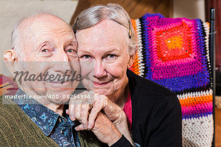 Happy elderly couple sitting in living-room with faces together