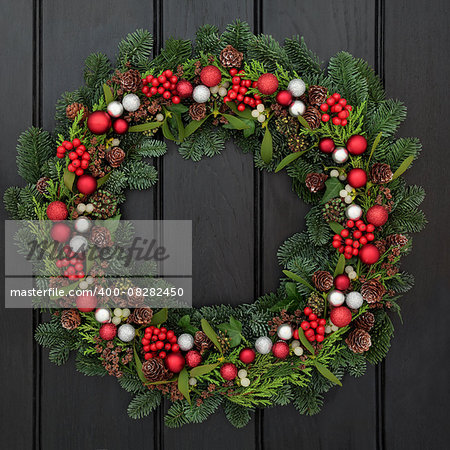Christmas wreath with red and silver bauble decorations, holly, mistletoe and winter greenery over dark blue oak front door background.