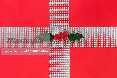 Christmas diamond bling and holly gift wrapping over red paper background.