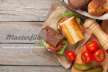 Two sandwiches with salad, ham, cheese and tomatoes on wooden table with copy space