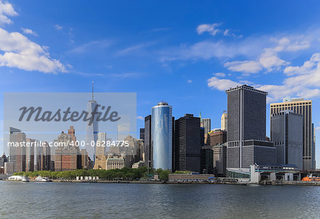 It's a view of Manhattan, New York City during the sunny day with a blue sky and riverside. There are many important building and places stated in that area which is a landmark of America about business and finance.