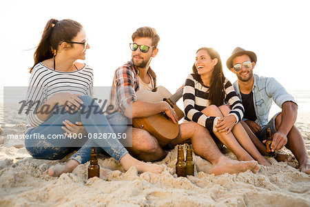 Friends having fun together at the beach, playing guitar and drinking beer