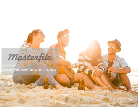 Friends having fun together at the beach, playing guitar and drinking beer