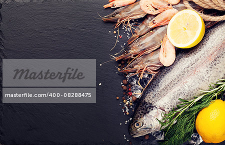 Fresh raw sea food with spices on black stone background. Top view with copy space. Toned