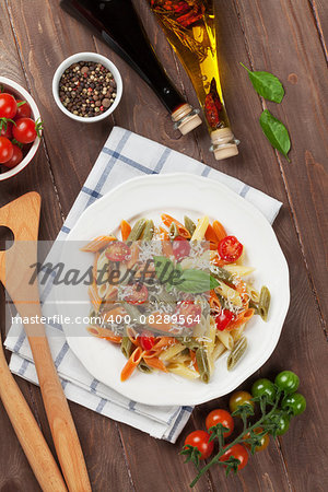 Colorful penne pasta with tomatoes and basil on wooden table. Top view