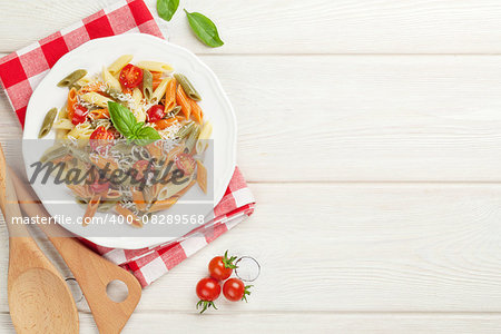 Colorful penne pasta with tomatoes and basil on wooden table. Top view with copy space