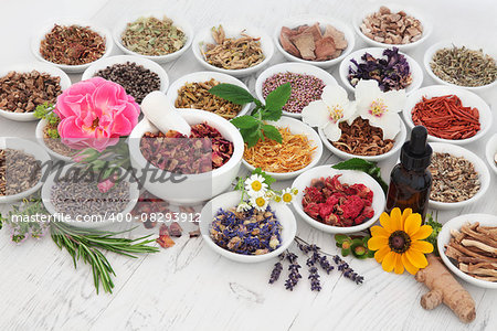 Natural herb and flower selection used in herbal medicine with medicinal dropper bottle and mortar with pestle  over distressed wooden background.