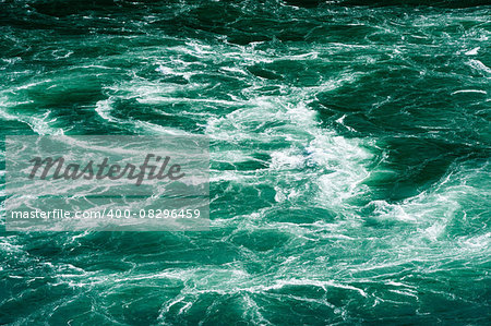 Abstract powerful white water currents churning in flowing green river.