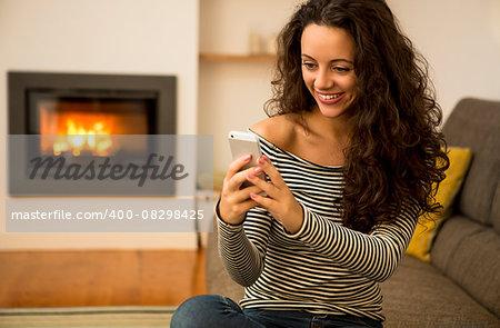 Beautiful woman using a cellphone at home at the warmth of a fireplace